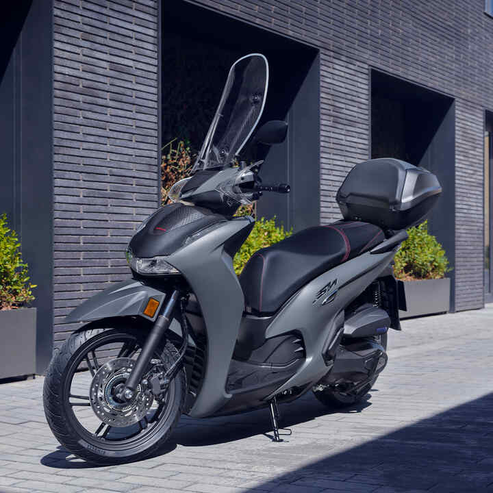 Přední tříčtvrtinový pohled na skútr Honda SH350i stojící před budovou